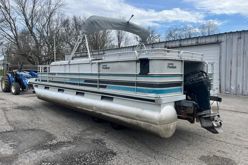 Slide: The Image of 1992 Harris FloteBote 240 Classic pontoon boat with canopy, parked near a tractor and building. - 4