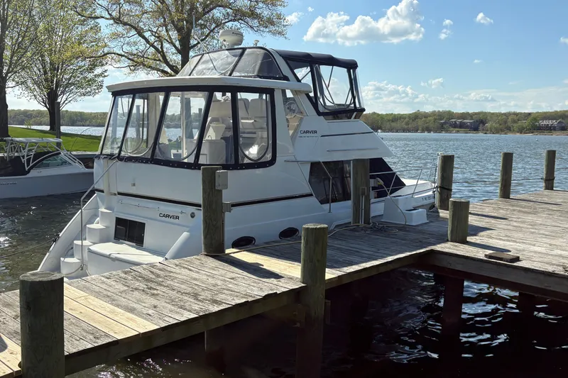 Slide: The Image of 2002 Carver 356 Aft Cabin Motor Yacht docked by a serene lake under a clear sky. - 5