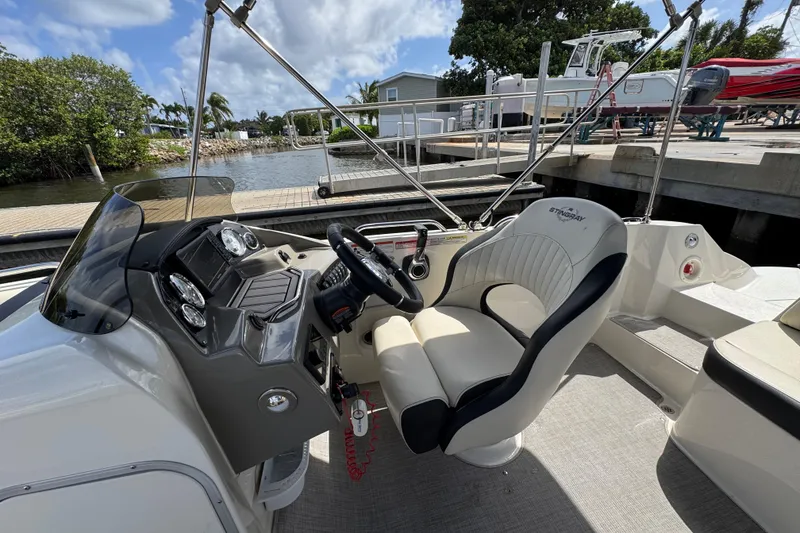 Slide: The Image of 2022 Stingray 192 SC boat interior with steering wheel and dashboard, docked by a scenic waterfront. - 9