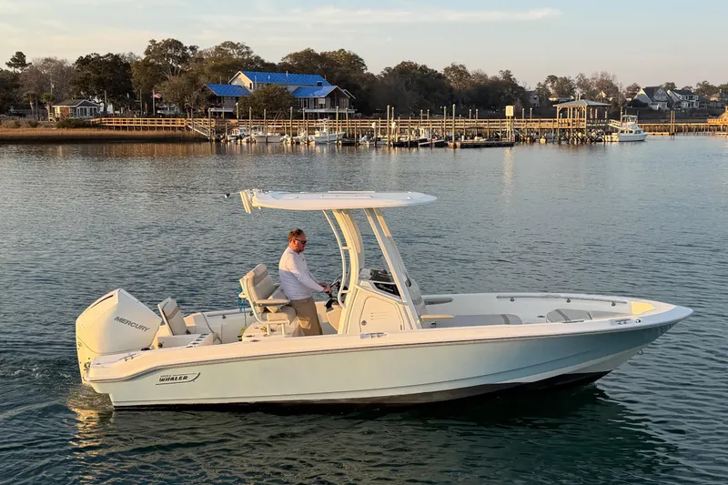 The Image of 2023 Boston Whaler 220 Dauntless boat cruising on calm waters near a dock. - 0