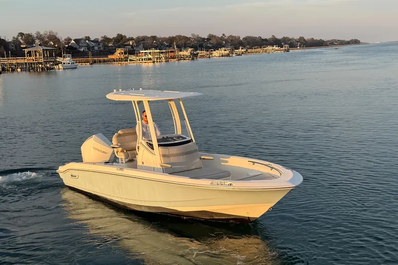 Slide: The Image of 2023 Boston Whaler 220 Dauntless boat cruising on calm waters near a coastal town. - 10