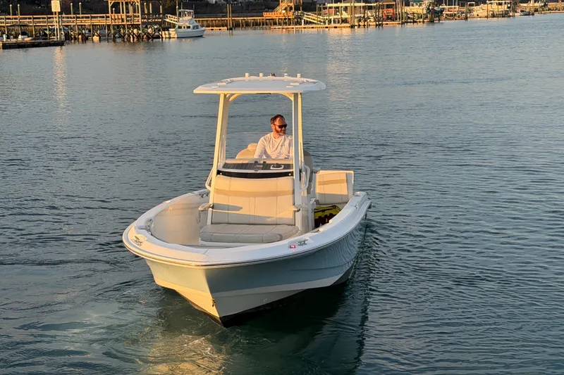 Slide: The Image of 2023 Boston Whaler 220 Dauntless boat cruising on calm water near a dock. - 12