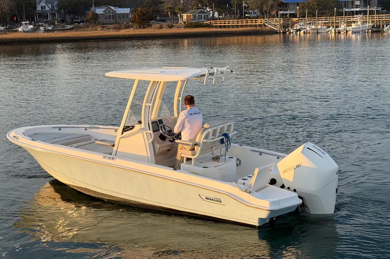 Slide: The Image of 2023 Boston Whaler 220 Dauntless boat cruising on calm waters near a dock. - 23
