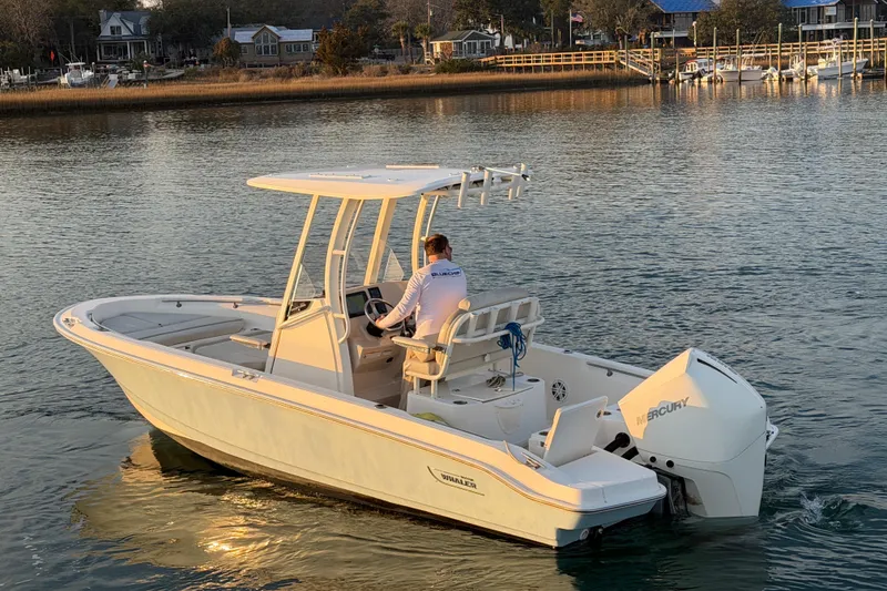 Slide: The Image of 2023 Boston Whaler 220 Dauntless boat cruising on calm water near a shoreline. - 24