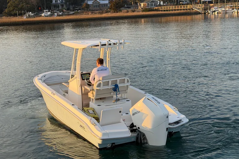 Slide: The Image of 2023 Boston Whaler 220 Dauntless boat cruising on calm water near a shoreline. - 25
