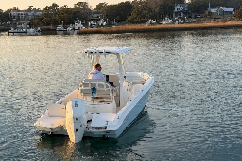Slide: The Image of 2023 Boston Whaler 220 Dauntless cruising on calm waters near a marina. - 30