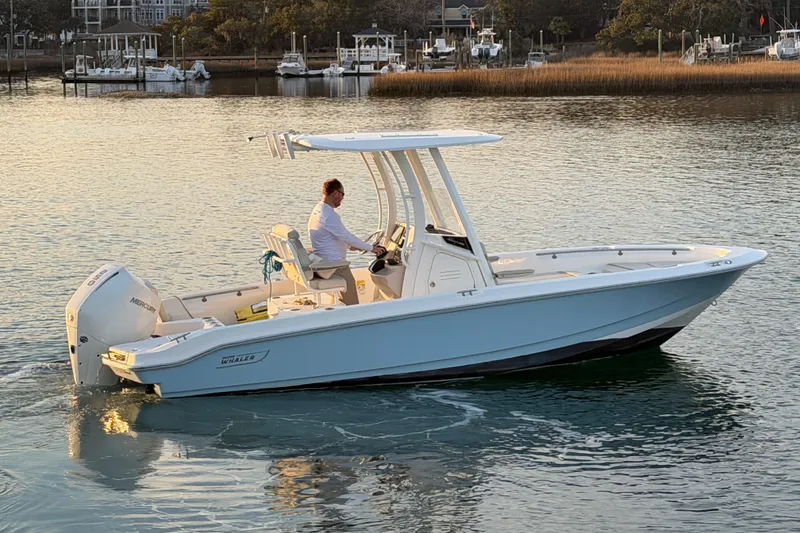 Slide: The Image of 2023 Boston Whaler 220 Dauntless boat cruising on calm water near a marina. - 34