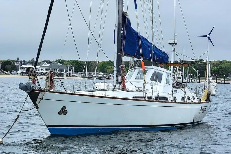 The Image of 1981 CT 49 sailboat anchored in a harbor with blue sails and wind turbine. - 0