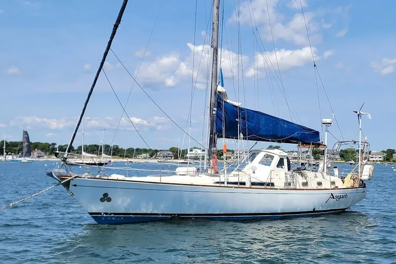 Slide: The Image of 1981 CT 47 sailboat with blue sails anchored in a scenic harbor. - 4