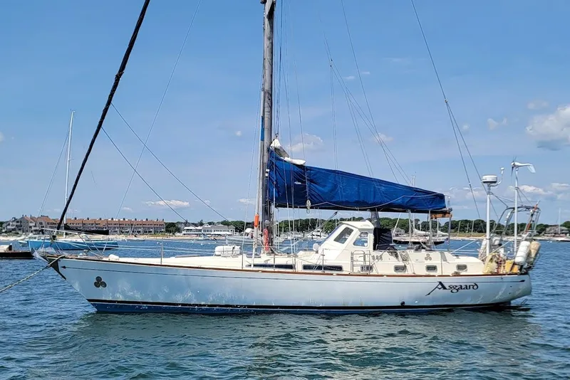 Slide: The Image of 1981 CT 47 sailboat with blue sails anchored in a scenic harbor. - 7