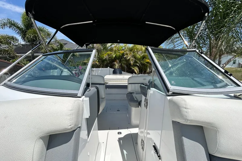 Slide: The Image of 2020 Cobalt 23SC boat interior with open windshield and seating, surrounded by palm trees. - 80