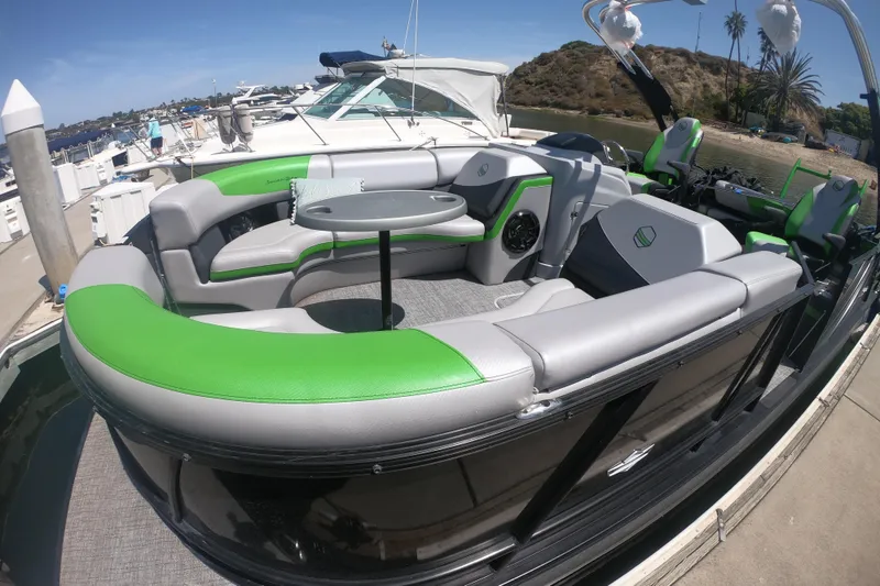 Slide: The Image of 2023 South Bay 525UL AR pontoon boat with green and gray seating, docked at a marina. - 2