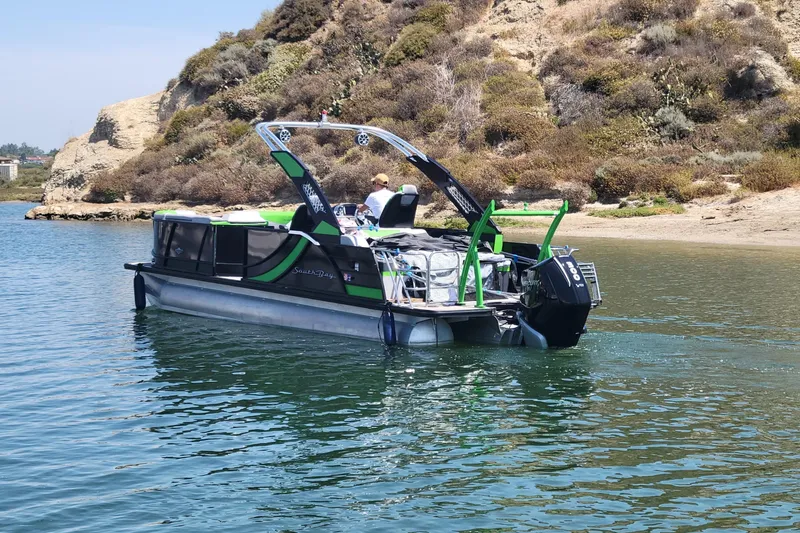 Slide: The Image of 2023 South Bay 525UL AR pontoon boat on calm water near rocky shoreline. - 9