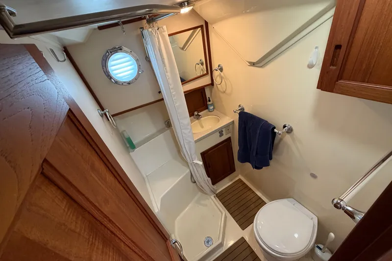 Slide: The Image of 2007 Nordic Tug 32 bathroom with shower, sink, and toilet, featuring wooden accents and porthole window. - 11