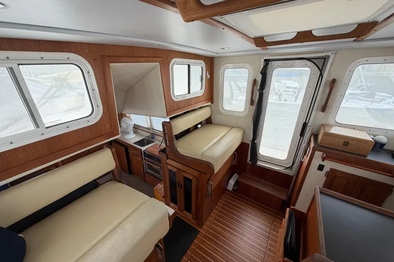 Slide: The Image of Interior of a 2007 Nordic Tug 32, featuring seating, windows, and a compact kitchen area. - 8