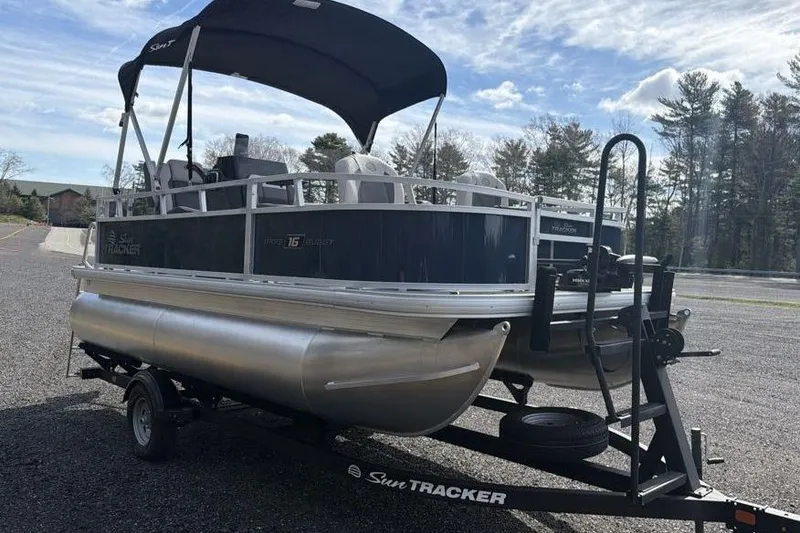 Slide: The Image of 2026 Sun Tracker Bass Buggy 16 XL Select pontoon boat on trailer, parked outdoors. - 3