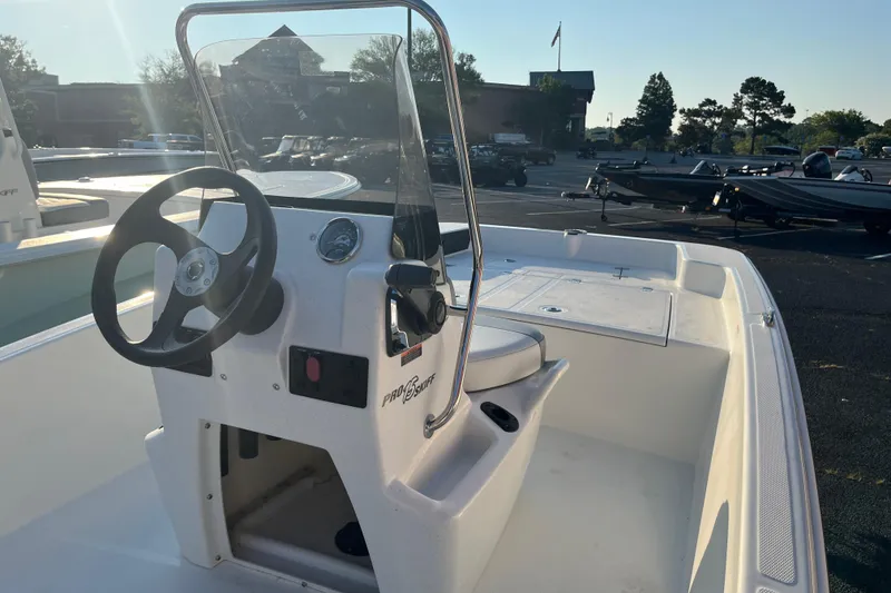 Slide: The Image of 2026 Mako Pro Skiff 15 CC boat interior with steering console in a parking lot. - 2