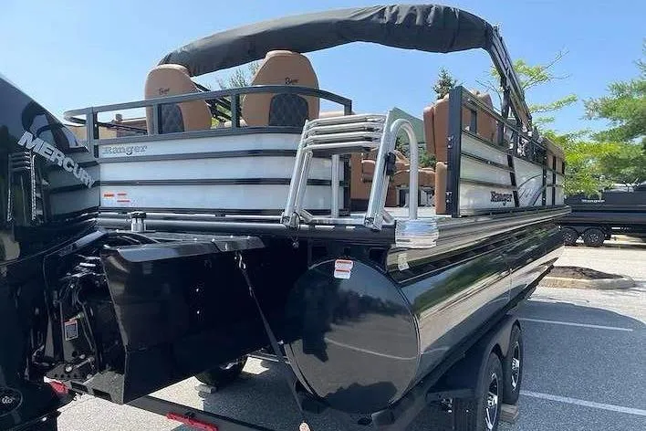 Slide: The Image of A modern Ranger 223FC pontoon boat with a black hull and beige interior, parked on a trailer. - 4