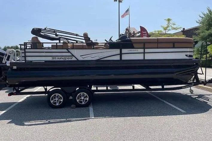 Slide: The Image of A Ranger 223FC pontoon boat on a trailer in a parking lot. It features a two-tone paint and canopy. - 1