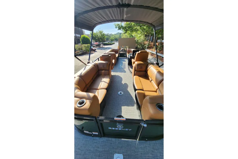 Slide: The Image of 2026 Regency 230 DL pontoon boat with tan seating and canopy, parked outdoors. - 5