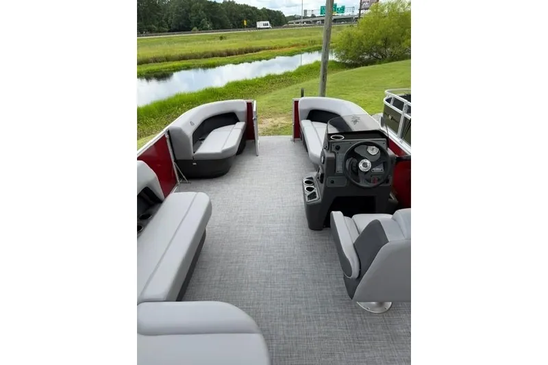 Slide: The Image of 2026 Sun Tracker Party Barge 16 DLX interior with seating and steering console, near a scenic waterway. - 16