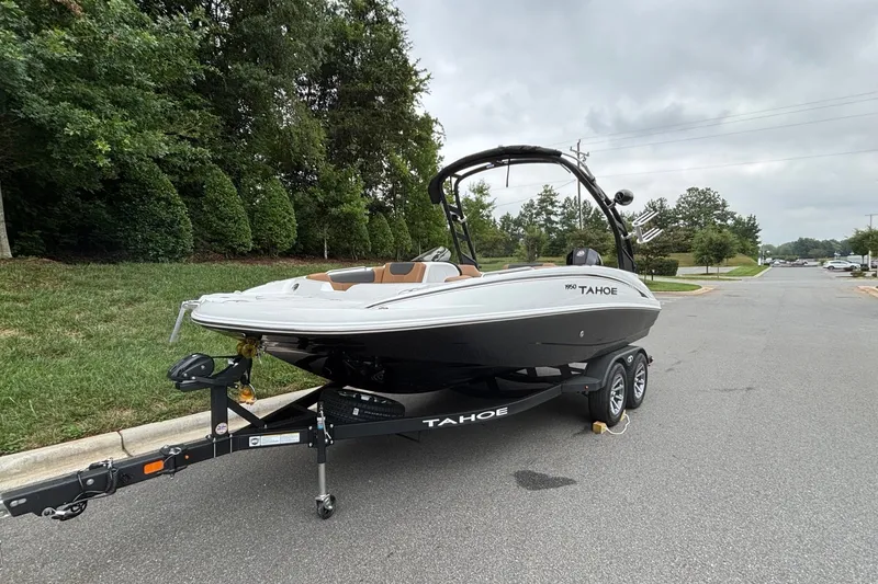 Slide: The Image of 2026 Tahoe 1950 boat on trailer, parked on a suburban street with lush greenery. - 2