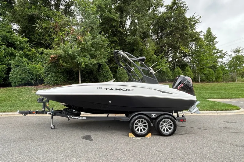 The Image of 2026 Tahoe 1950 boat on trailer, parked on road with lush green background. - 0
