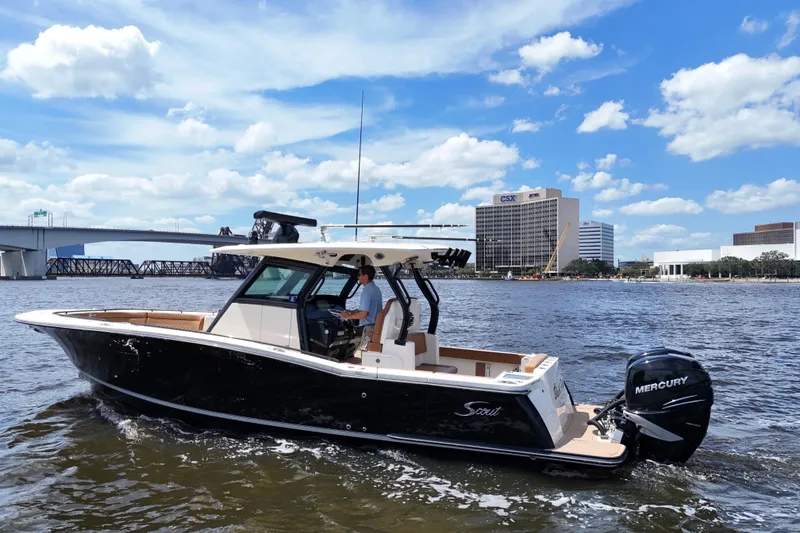 Slide: The Image of 2021 Scout 330 LXF boat cruising on a sunny day near modern waterfront buildings. - 10
