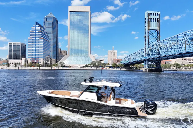 Slide: The Image of 2021 Scout 330 LXF boat cruising near city skyline and blue bridge on a sunny day. - 18