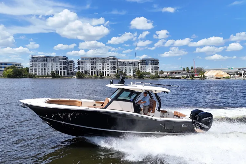 Slide: The Image of 2021 Scout 330 LXF boat on water with city skyline and bridge in background. - 2
