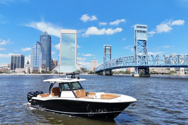 Slide: The Image of 2021 Scout 330 LXF boat cruising on a river with city skyline backdrop. - 3