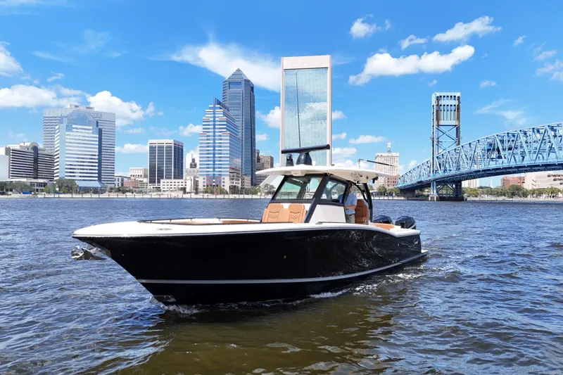Slide: The Image of 2021 Scout 330 LXF boat cruising on a river with city skyline backdrop. - 4