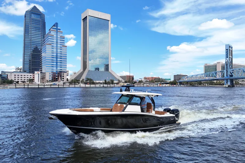 Slide: The Image of 2021 Scout 330 LXF boat cruising on a river with city skyline backdrop. - 6