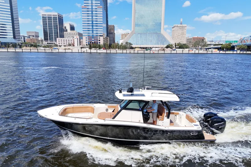 Slide: The Image of 2021 Scout 330 LXF boat cruising on a river with city skyline backdrop. - 95