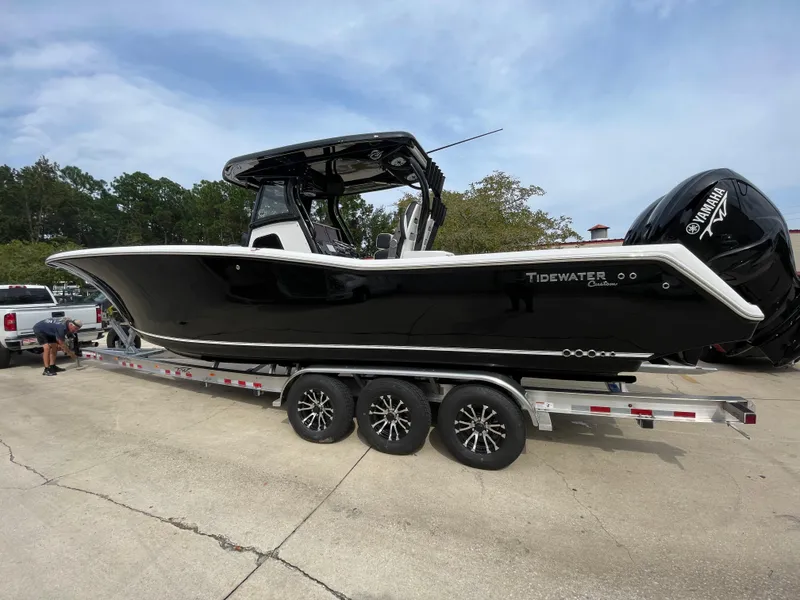 The Image of 2023 Tidewater 320 CC Adventure boat on a trailer, black hull, triple-axle wheels. - 0
