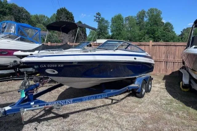 The Image of 2005 Crownline 202 BR boat on trailer, parked outdoors near wooden fence. - 1