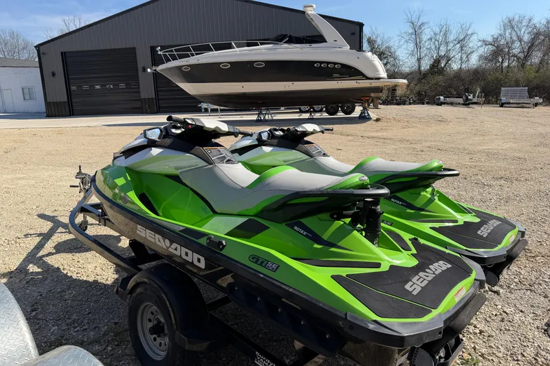Slide: The Image of Two green 2014 Sea-Doo GTI 130 jet skis on a trailer, parked near a boat. - 6