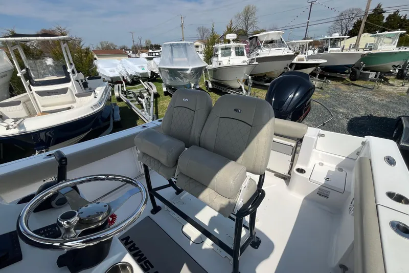 Slide: The Image of 2022 Sportsman Open 242 Center Console boat with dual seats and steering wheel, parked among other boats. - 14