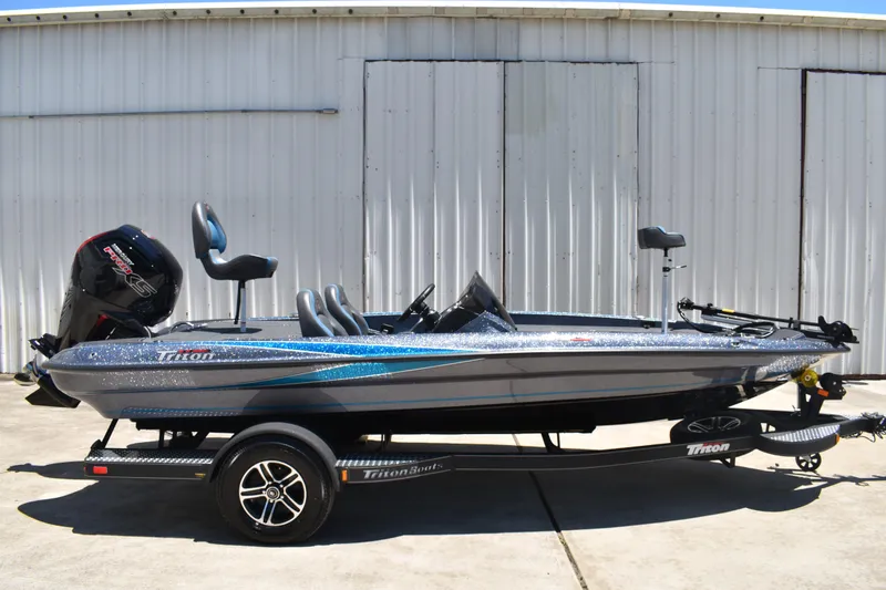 The Image of 2026 Triton 179 TrX bass boat with trailer, parked outdoors near a metal building. - 0