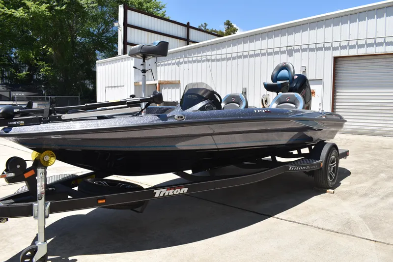 Slide: The Image of 2026 Triton 179 TrX bass boat on trailer, parked outdoors near a metal building. - 10