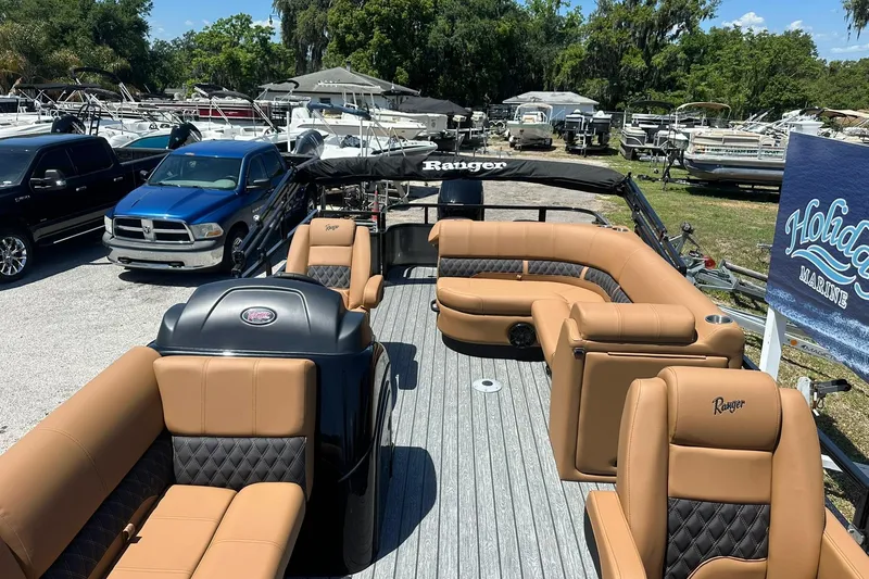 Slide: The Image of 2026 Ranger Reata 220FC pontoon boat with tan seating, parked at a marina. - 7