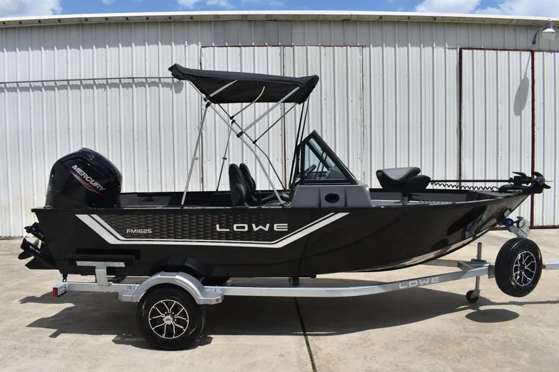 The Image of 2026 Lowe Fishing Machine 1625WT boat on trailer, featuring sleek black design and Mercury outboard motor. - 2