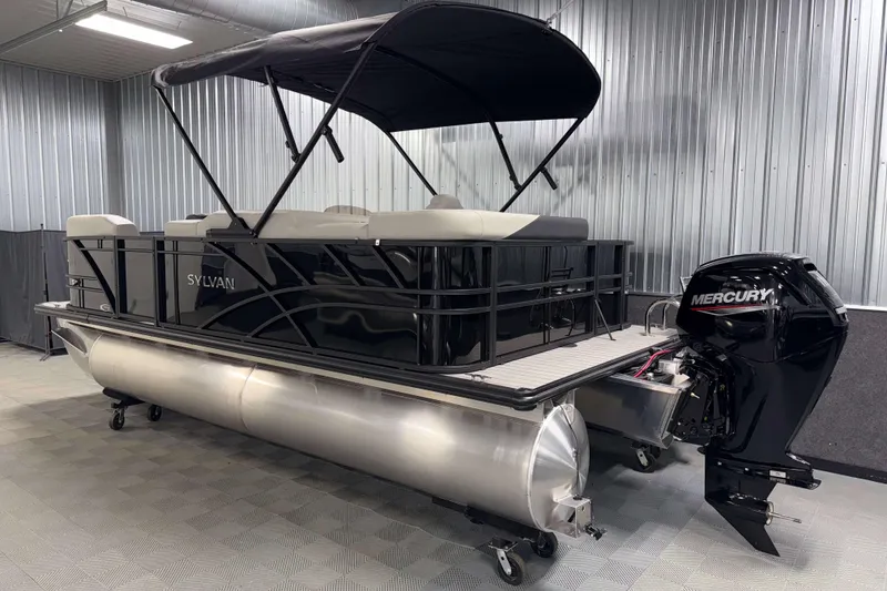 Slide: The Image of 2026 Sylvan Mirage 8520 Cruise pontoon boat with Mercury outboard in a metal-walled showroom. - 23