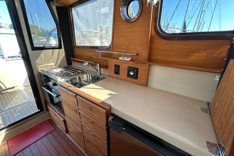 Slide: The Image of 2020 Ranger Tugs R-27 boat interior kitchen with sink, stove, and wooden cabinetry. - 6