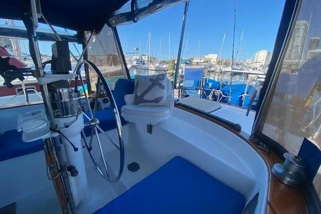 Slide: The Image of Cockpit of 1982 Endeavour 40 sailboat with marina view, featuring blue seating and steering wheel. - 18