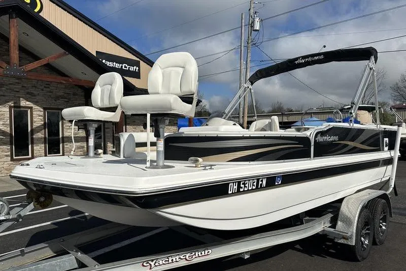Slide: The Image of 2026 Hurricane FunDeck 196 RE boat on trailer, parked outside a building under cloudy sky. - 6