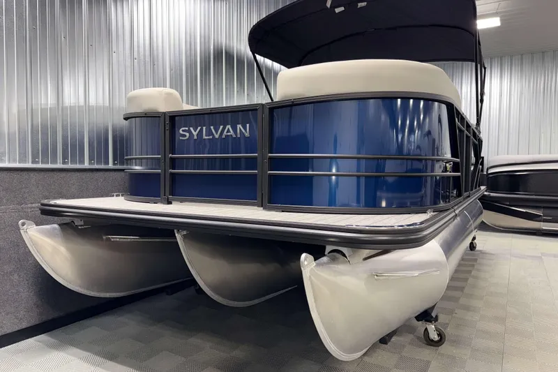 Slide: The Image of 2026 Sylvan Mirage 8520 LZ PTS Tritoon in showroom, featuring sleek blue design and sturdy pontoons. - 18
