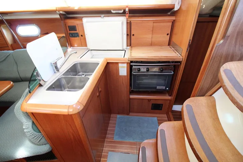 Slide: The Image of 2004 Jeanneau Sun Odyssey 35 yacht interior kitchen with sink, stove, and wooden cabinetry. - 18