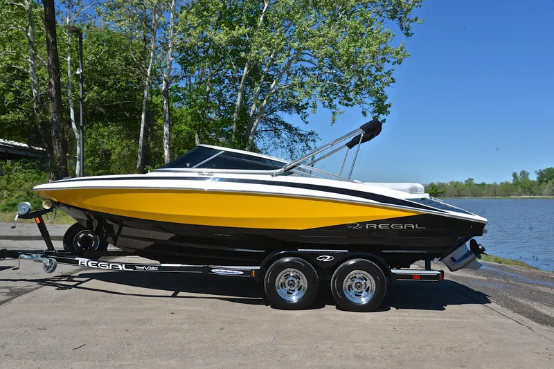 Slide: The Image of 2014 Regal 2100 boat on trailer by a lake, surrounded by trees. - 11