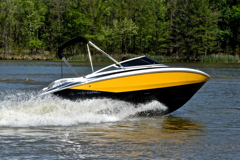 Slide: The Image of 2014 Regal 2100 boat cruising on a lake with lush green forest backdrop. - 5